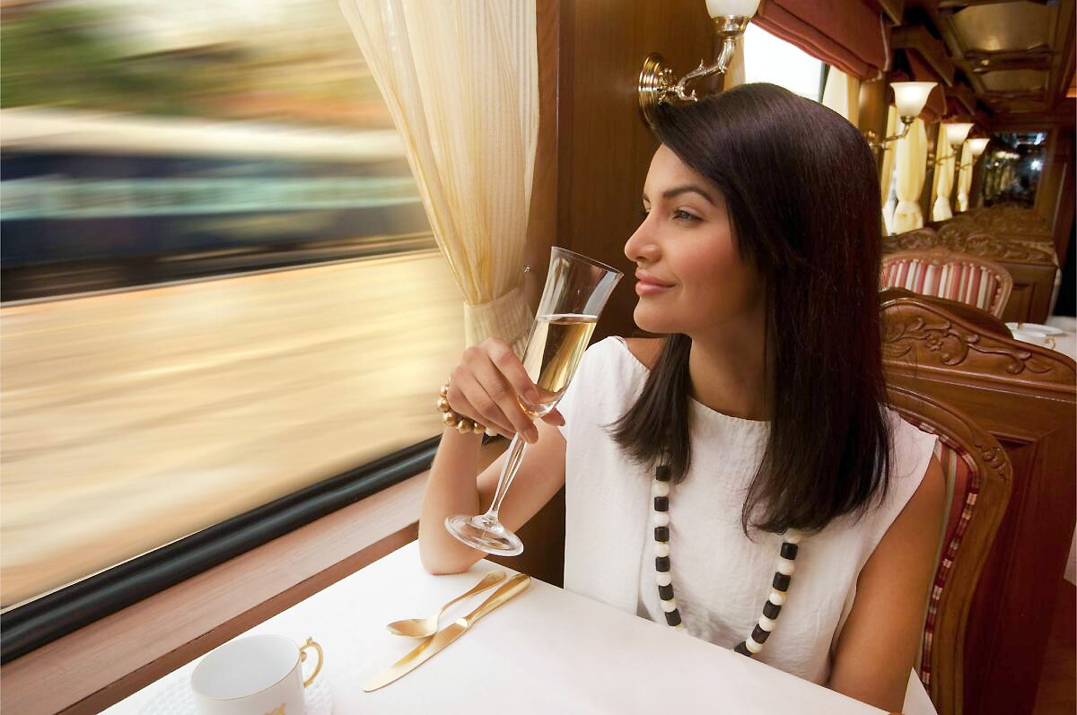 Indian luxury train in deep maroon and gold at sunset, guests boarding with staff in traditional attire on the platform