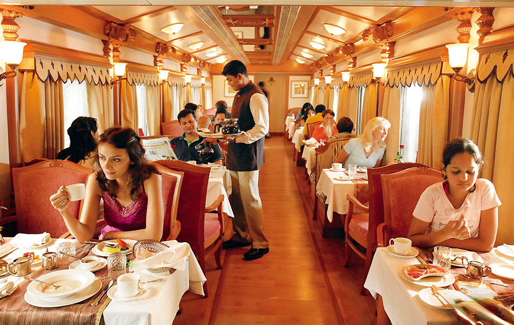 Indian luxury train in deep maroon and gold at sunset, guests boarding with staff in traditional attire on the platform